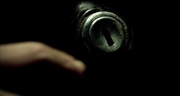 Movie still from “Wolf Creek” (2005), directed by Greg McLean – A finger is pointing to a lock on a door knob; Extreme Close Up shot, Overhead angle