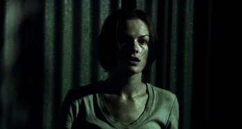 Movie still from “Wolf Creek” (2005), directed by Greg McLean – A woman in a white shirt is in a dark room; Medium shot, Low angle