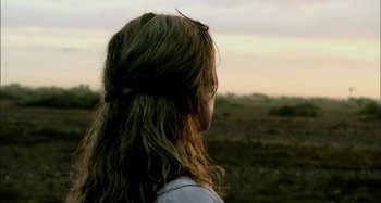 Movie still from “Wolf Creek” (2005), directed by Greg McLean – A woman with long brown hair standing in a field; Close Up shot, Over the shoulder angle