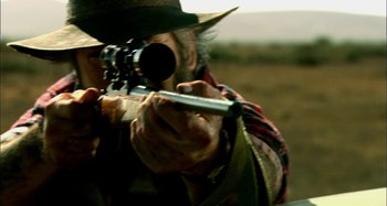 Movie still from “Wolf Creek” (2005), directed by Greg McLean – A man with a rifle aiming at something in the distance; Extreme Close Up shot, Over the shoulder angle