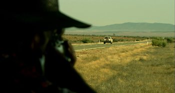 Movie still from “Wolf Creek” (2005), directed by Greg McLean – A man taking a picture of a car on the side of the road; Extreme Wide shot, Over the shoulder angle