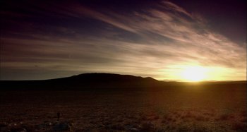 Movie still from “Wolf Creek” (2005), directed by Greg McLean – The sun is setting over a field of grass and hills; Extreme Wide shot, Low angle