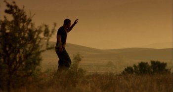 Movie still from “Wolf Creek” (2005), directed by Greg McLean – A man standing in a field with his hand raised; Wide shot, Low angle