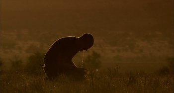 Movie still from “Wolf Creek” (2005), directed by Greg McLean – A man sitting in the grass drinking from a water faucet; Medium shot, Low angle