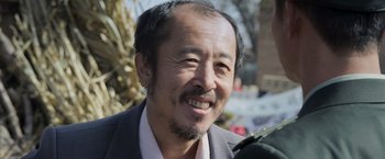 Movie still from “Wolf Warrior 2” (2017), directed by Jing Wu – A person wearing a suit and smiling; Close Up shot, Over the shoulder angle