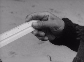 Movie still from “Woman in the Dunes” (1964), directed by Hiroshi Teshigahara – A person holding a ruler in their hand; Extreme Close Up shot, High angle