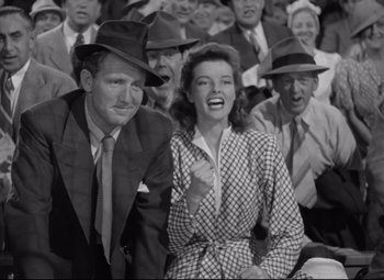 Movie still from “Woman of the Year” (1942), directed by George Stevens – A man and a woman are sitting in front of a group of people; Medium shot, Low angle