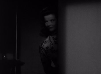 Movie still from “Woman of the Year” (1942), directed by George Stevens – A black - and - white photo of a woman standing in front of a wall; Medium shot, Over the shoulder angle