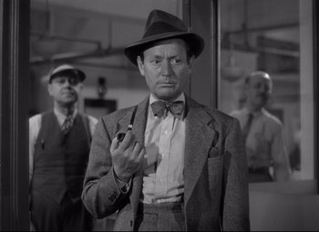 Movie still from “Woman of the Year” (1942), directed by George Stevens – An old photo of a man in a suit and tie holding a pipe; Medium shot, Low angle