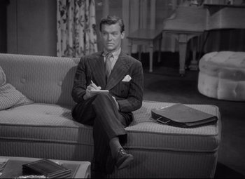 Movie still from “Woman of the Year” (1942), directed by George Stevens – A black and white photo of a man sitting on a couch; Medium shot, High angle