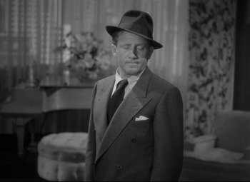 Movie still from “Woman of the Year” (1942), directed by George Stevens – A man in a suit and hat standing in front of a window; Close Up shot, High angle