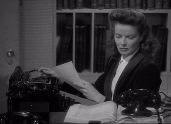 Movie still from “Woman of the Year” (1942), directed by George Stevens – A woman sitting at a desk with a book and a typewriter; Medium shot, High angle