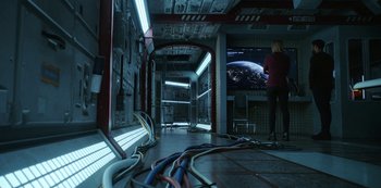 Movie still from “Another Life” (2019), created by Aaron Martin – A woman standing in front of a television in a room; Wide shot, High angle