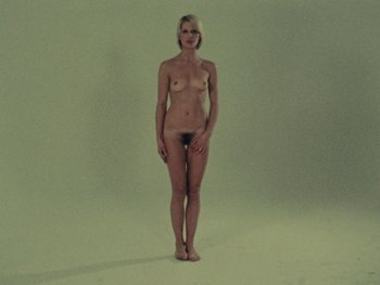 Movie still from “Women Reply” (1975), directed by Agnès Varda – A woman standing naked in a room with a green background; Wide shot, High angle