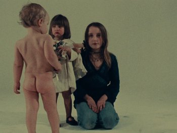 Movie still from “Women Reply” (1975), directed by Agnès Varda – A woman kneeling on the ground next to two small children; Medium shot, High angle