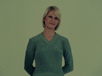 Movie still from “Women Reply” (1975), directed by Agnès Varda – A woman in a green shirt posing for a picture; Medium shot, Low angle