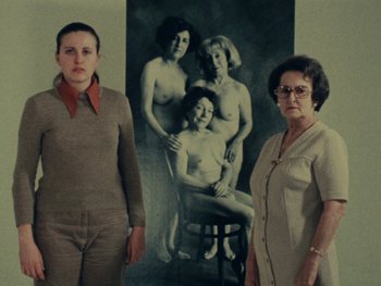 Movie still from “Women Reply” (1975), directed by Agnès Varda – Two women standing in front of a picture of a family; Medium shot, Low angle