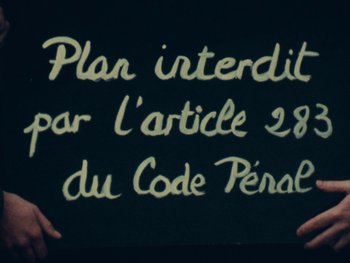 Movie still from “Women Reply” (1975), directed by Agnès Varda – Two hands holding a chalkboard that reads " plan interdit par l ' article 2 8 du code péraire "; Extreme Close Up shot, High angle
