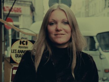 Movie still from “Women Reply” (1975), directed by Agnès Varda – A woman with long blonde hair standing in front of a street sign; Close Up shot, Low angle