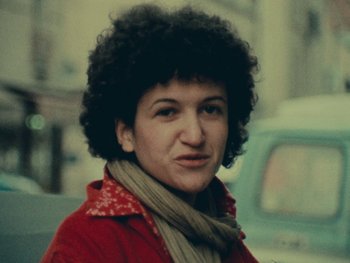 Movie still from “Women Reply” (1975), directed by Agnès Varda – A woman in a red jacket and a scarf; Close Up shot, High angle