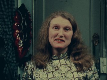 Movie still from “Women Reply” (1975), directed by Agnès Varda – A woman with long brown hair wearing a brown and white shirt; Close Up shot, Over the shoulder angle