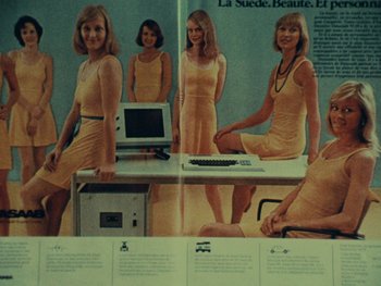Movie still from “Women Reply” (1975), directed by Agnès Varda – A group of women standing next to a computer desk; Wide shot, Overhead angle