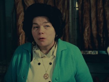 Movie still from “Women Reply” (1975), directed by Agnès Varda – A woman wearing a green jacket and a black hat; Close Up shot, Low angle