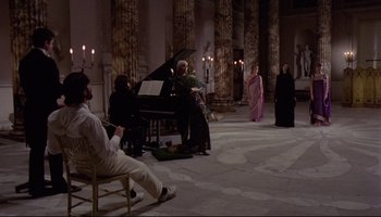 Movie still from “Women in Love” (1969), directed by Ken Russell – A group of people sitting around a grand piano; Wide shot, High angle