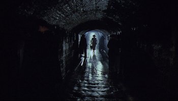 Movie still from “Women in Love” (1969), directed by Ken Russell – A person is walking down a dark path in a tunnel; Wide shot, High angle