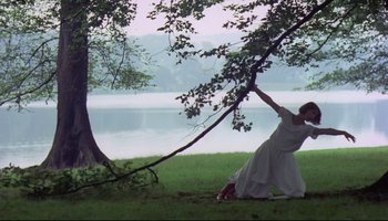 Movie still from “Women in Love” (1969), directed by Ken Russell – A woman in a white dress standing next to a tree; Wide shot, Low angle