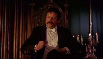 Movie still from “Women in Love” (1969), directed by Ken Russell – A man in a tuxedo sitting in a chair with candles; Medium shot, Low angle