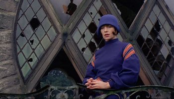 Movie still from “Women in Love” (1969), directed by Ken Russell – A woman wearing a blue hat is standing outside; Medium shot, Low angle