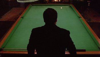 Movie still from “Women in Love” (1969), directed by Ken Russell – A man sitting in front of a pool table; Medium shot, Over the shoulder angle