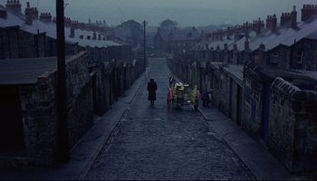Movie still from “Women in Love” (1969), directed by Ken Russell – A person walking down a street near a row of houses; Extreme Wide shot, High angle