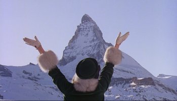 Movie still from “Women in Love” (1969), directed by Ken Russell – A person with their hands up in front of a snow covered mountain; Extreme Wide shot, Low angle