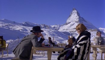 Movie still from “Women in Love” (1969), directed by Ken Russell – A group of people sitting at a table in the middle of the snow; Wide shot, Over the shoulder angle