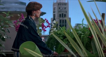 Movie still from “Women on the Verge of a Nervous Breakdown” (1988), directed by Pedro Almodóvar – A woman sitting on top of a table next to plants; Medium shot, Low angle