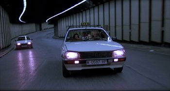 Movie still from “Women on the Verge of a Nervous Breakdown” (1988), directed by Pedro Almodóvar – A white taxi driving down a street at night; Wide shot, Low angle