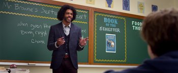 Movie still from “Wonder” (2017), directed by Stephen Chbosky – A man standing in front of chalkboards with a book of the semester written on it; Medium shot, Over the shoulder angle