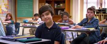 Movie still from “Wonder” (2017), directed by Stephen Chbosky – A boy sitting at a desk in front of other students; Medium shot, High angle