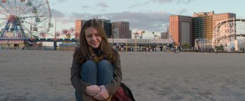 Movie still from “Wonder” (2017), directed by Stephen Chbosky – A young woman sitting on the beach in front of a ferris wheel; Medium shot, Low angle