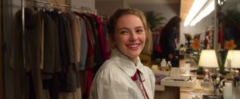 Movie still from “Wonder” (2017), directed by Stephen Chbosky – A young woman smiling for the camera in front of clothes; Close Up shot, Over the shoulder angle