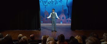 Movie still from “Wonder” (2017), directed by Stephen Chbosky – A man wearing a suit and tie standing on a stage; Wide shot, Over the shoulder angle