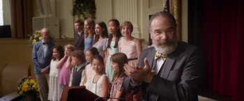 Movie still from “Wonder” (2017), directed by Stephen Chbosky – A group of people standing next to each other in front of a podium; Medium shot, Over the shoulder angle