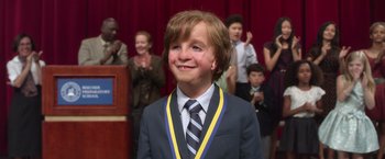 Movie still from “Wonder” (2017), directed by Stephen Chbosky – A young boy in a suit and tie smiling for the camera; Close Up shot, Over the shoulder angle