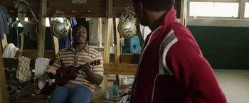 Movie still from “Woodlawn” (2015), directed by Jon Erwin – A man sitting on the ground playing a guitar; Medium shot, High angle