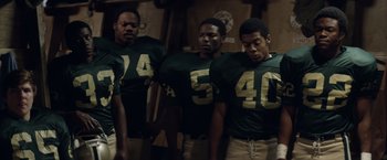 Movie still from “Woodlawn” (2015), directed by Jon Erwin – A group of men standing next to each other in football uniforms; Medium shot, High angle