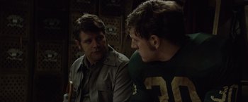 Movie still from “Woodlawn” (2015), directed by Jon Erwin – Two men are sitting next to each other; Medium shot, Over the shoulder angle
