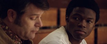 Movie still from “Woodlawn” (2015), directed by Jon Erwin – Two men sitting next to each other in front of a wooden wall; Close Up shot, Over the shoulder angle