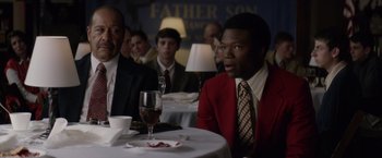 Movie still from “Woodlawn” (2015), directed by Jon Erwin – A group of people sitting at a table with a glass of red wine; Medium shot, Over the shoulder angle